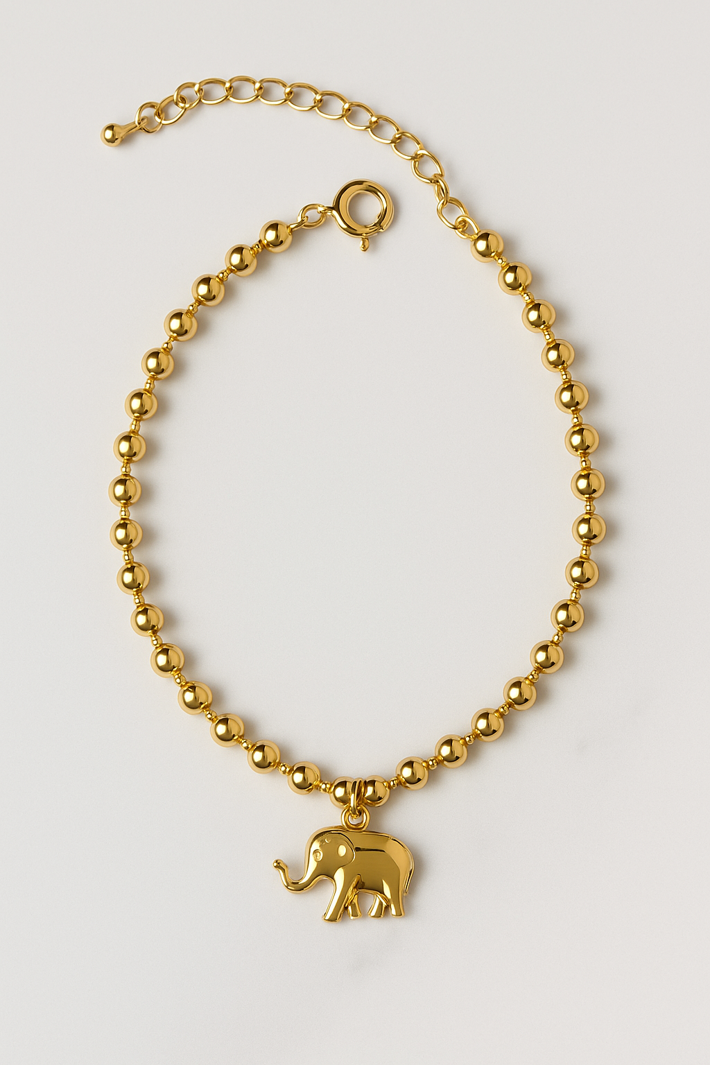 Chevillère dorée en acier inoxydable avec pendentif éléphant, posée à plat sur fond clair, photo produit e-shop MOUN’ »