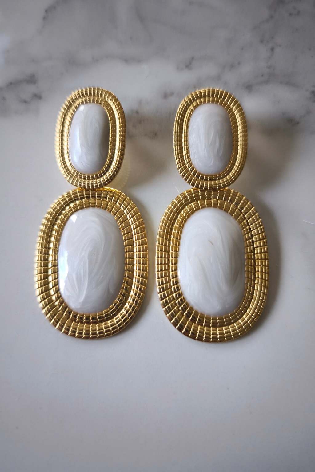 Boucles d’oreilles Likasi Blanche en acier doré et résine ivoire marbrée, présentation sur fond clair.