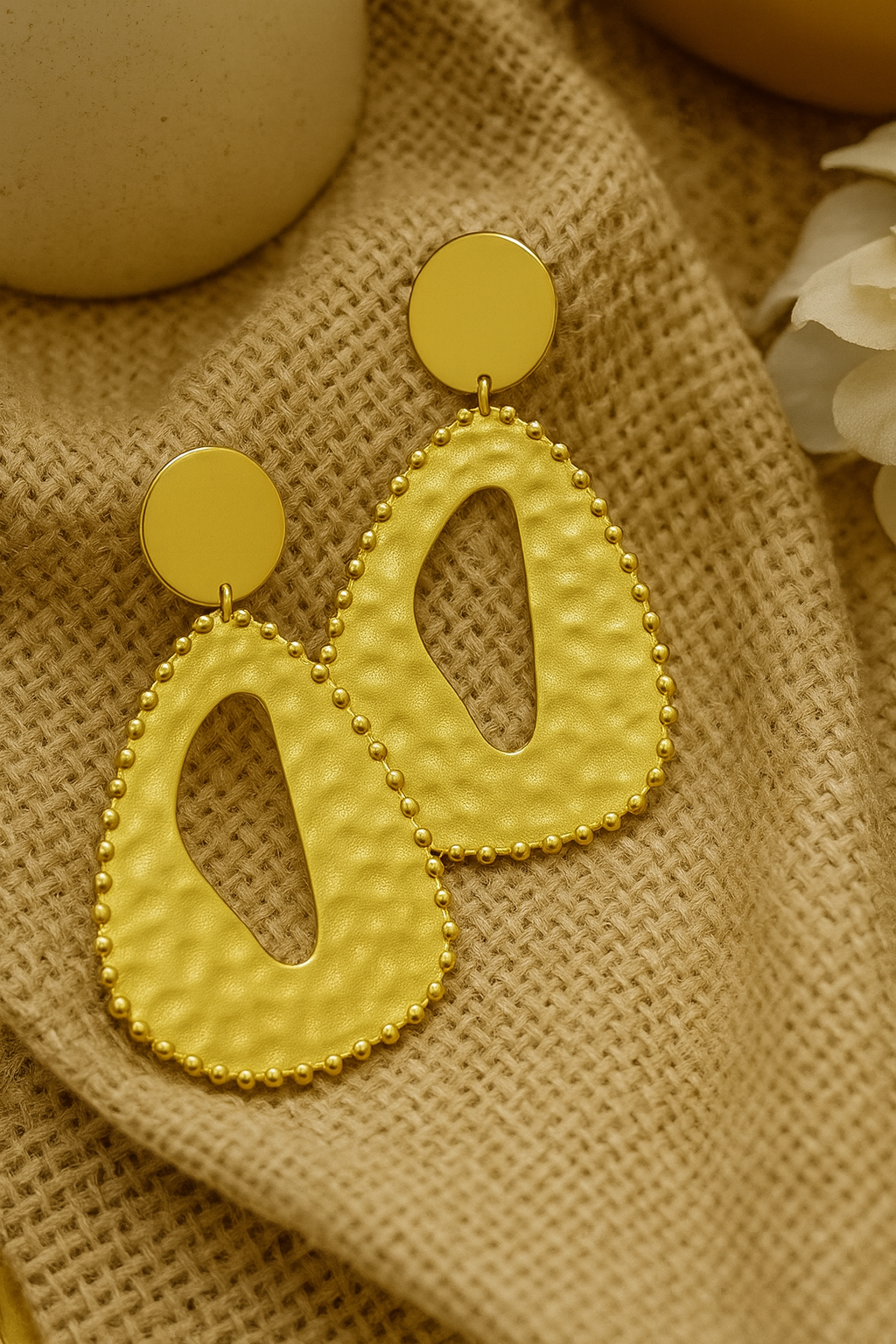 Boucles d’oreilles dorées Zama en acier inoxydable, design goutte martelée avec perles en relief, présentées sur fond texturé chic, bijoux tendance afro-chic MOUN’.