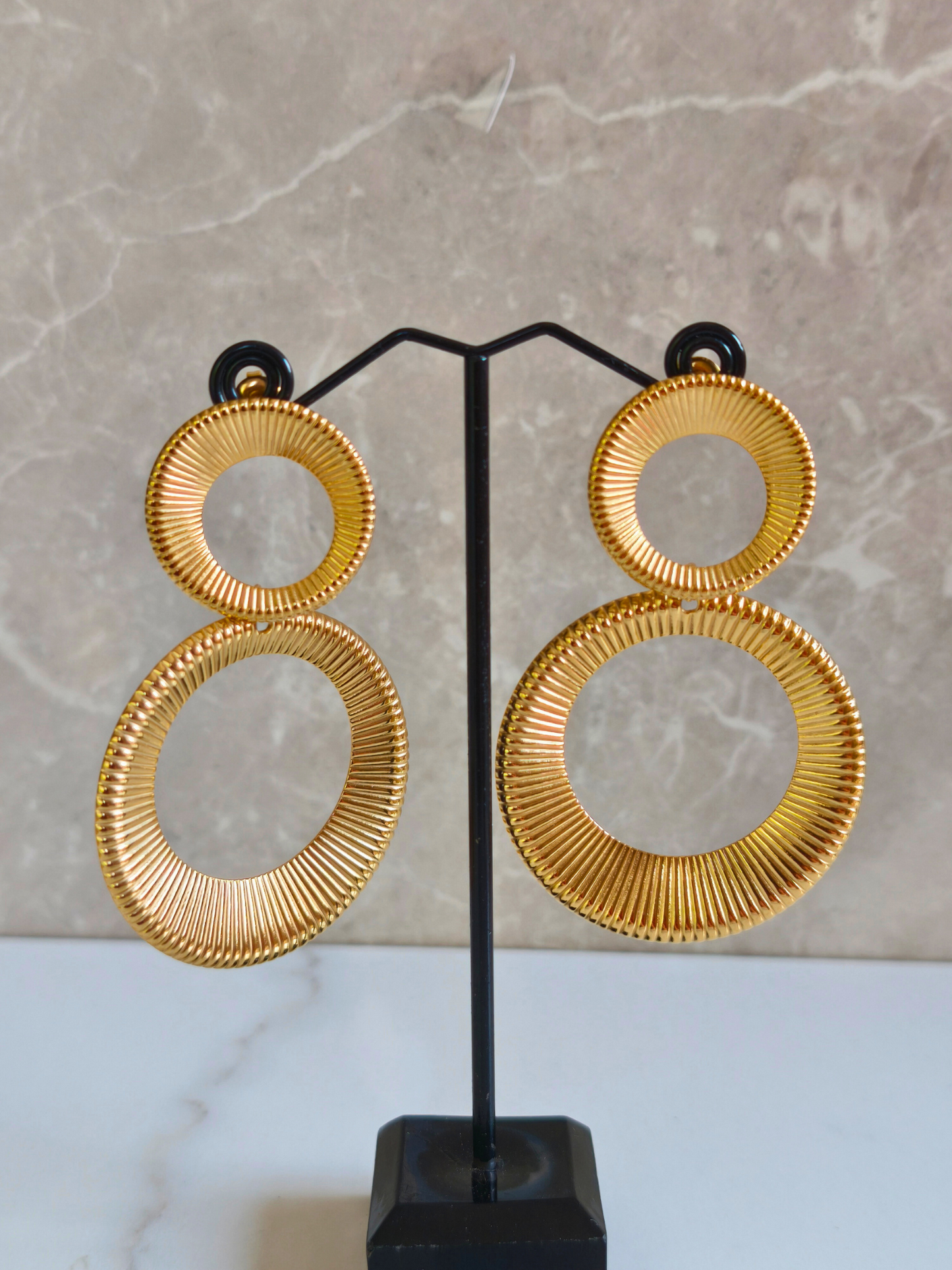 Boucles d’oreilles Asiba en acier doré texturé sur leur support, deux cercles entrelacés