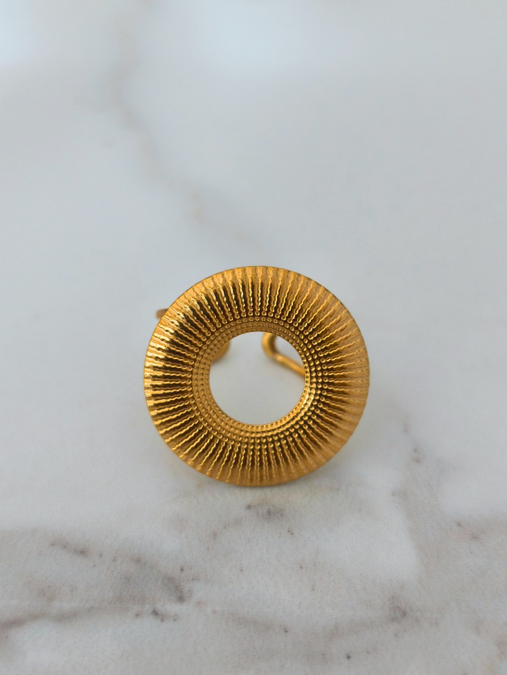 Bague Zuri en acier inoxydable doré, design circulaire texturé, posée sur fond ivoire neutre.