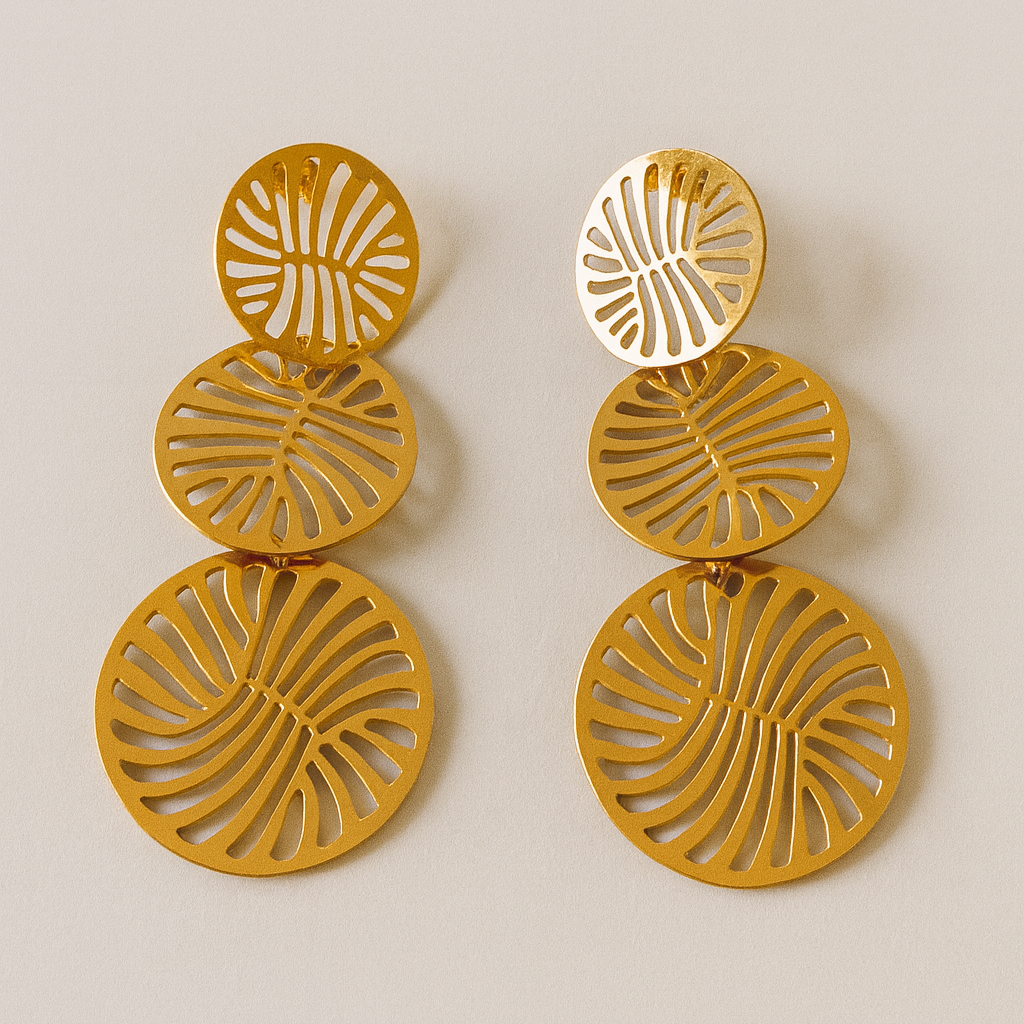 Boucles d’oreilles Tambira en acier doré, trois cercles ajourés superposés au motif graphique, présentées sur fond clair.
