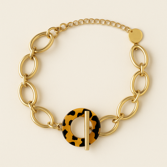 Bracelet Ndomo – mailles dorées en acier inoxydable et fermoir écaille, photographié sur fond beige chaud texturé.