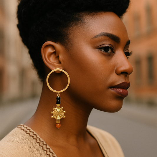 Boucles d’oreilles Nalengo portées par une femme noire, créoles dorées ornées d’un pendentif en spirale avec perles noires et orange, en extérieur urbain.