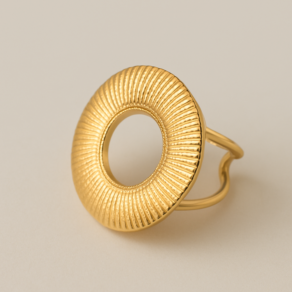 Bague Zuri en acier inoxydable doré, design circulaire texturé, posée sur fond ivoire neutre.